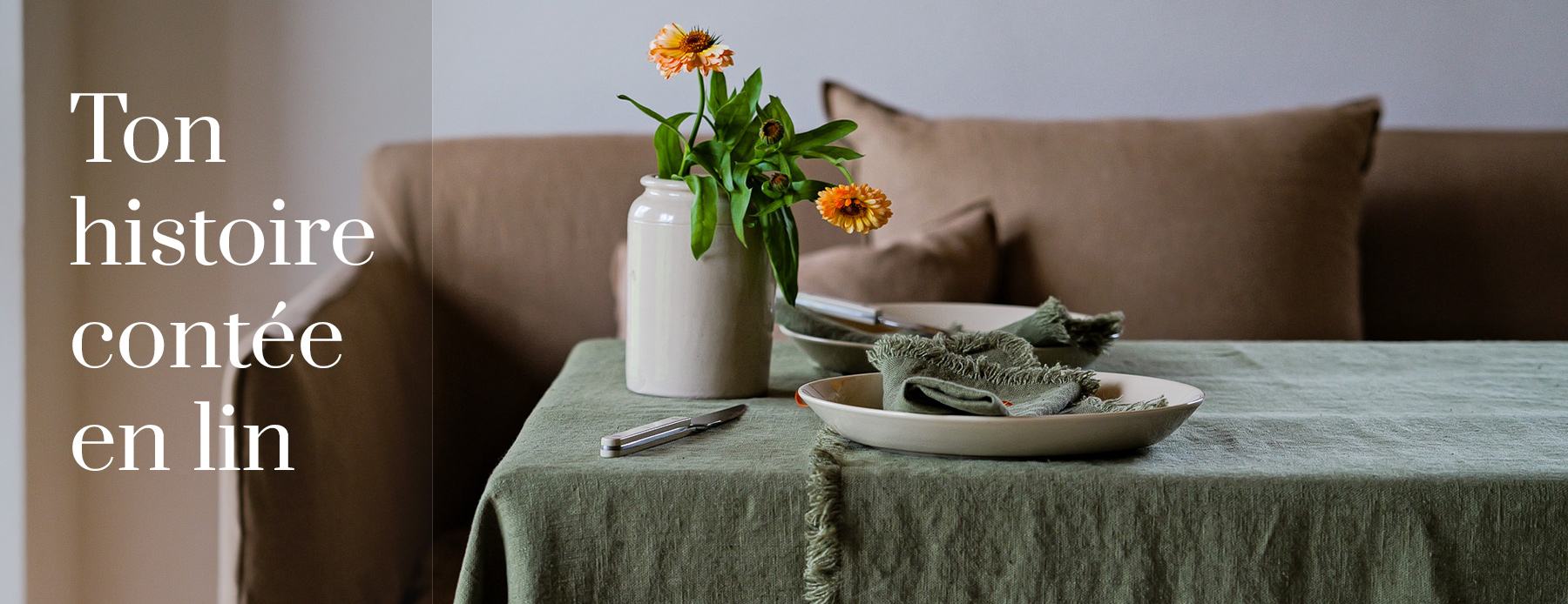 Ton histoire contée en lin – nappe en lin vert avec des serviettes et des fleurs d’automne devant un canapé.