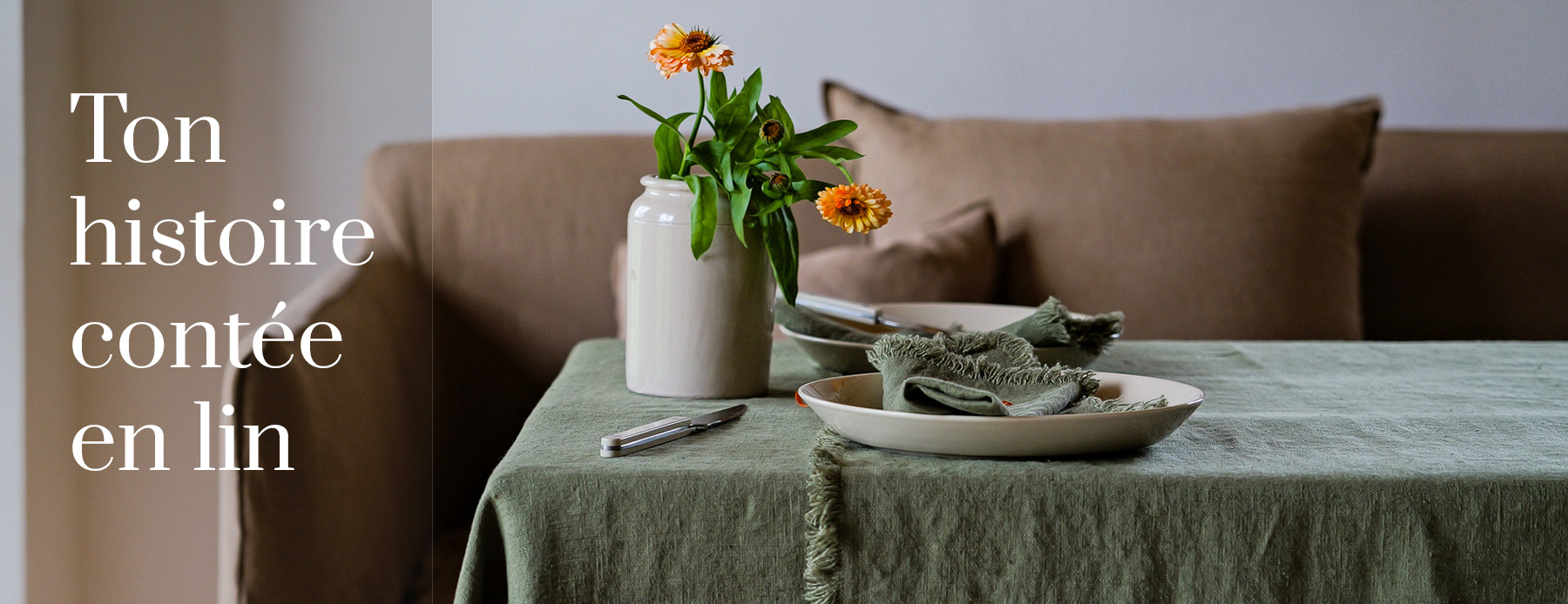 Ton histoire contée en lin – nappe en lin vert avec des serviettes et des fleurs d’automne devant un canapé.