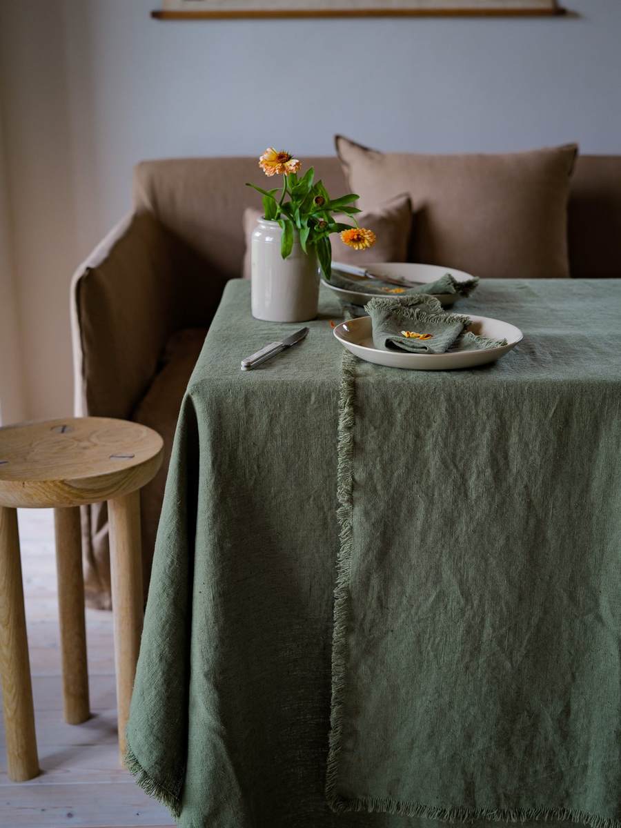 Nappe en lin vert olive à franges avec assiettes crème et vase de fleurs