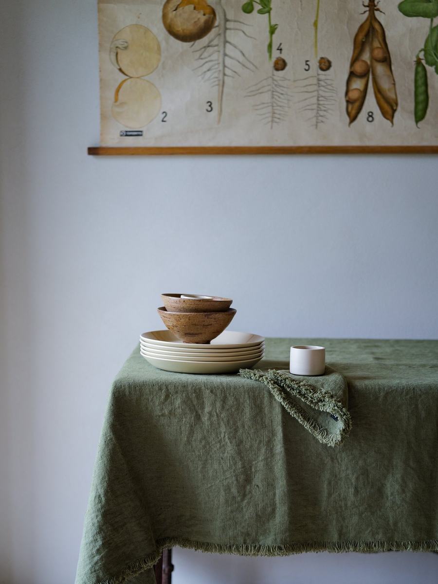 Assiettes crème et bols en bois sur du lin vert olive
