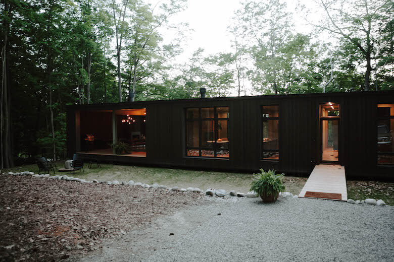 Maison collaborative Birch Le de Hygge Supply éclairée parmi les arbres au crépuscule