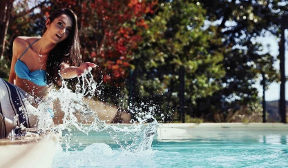 Femme assise au bord d’une piscine avec une serviette de plage en lin rayée